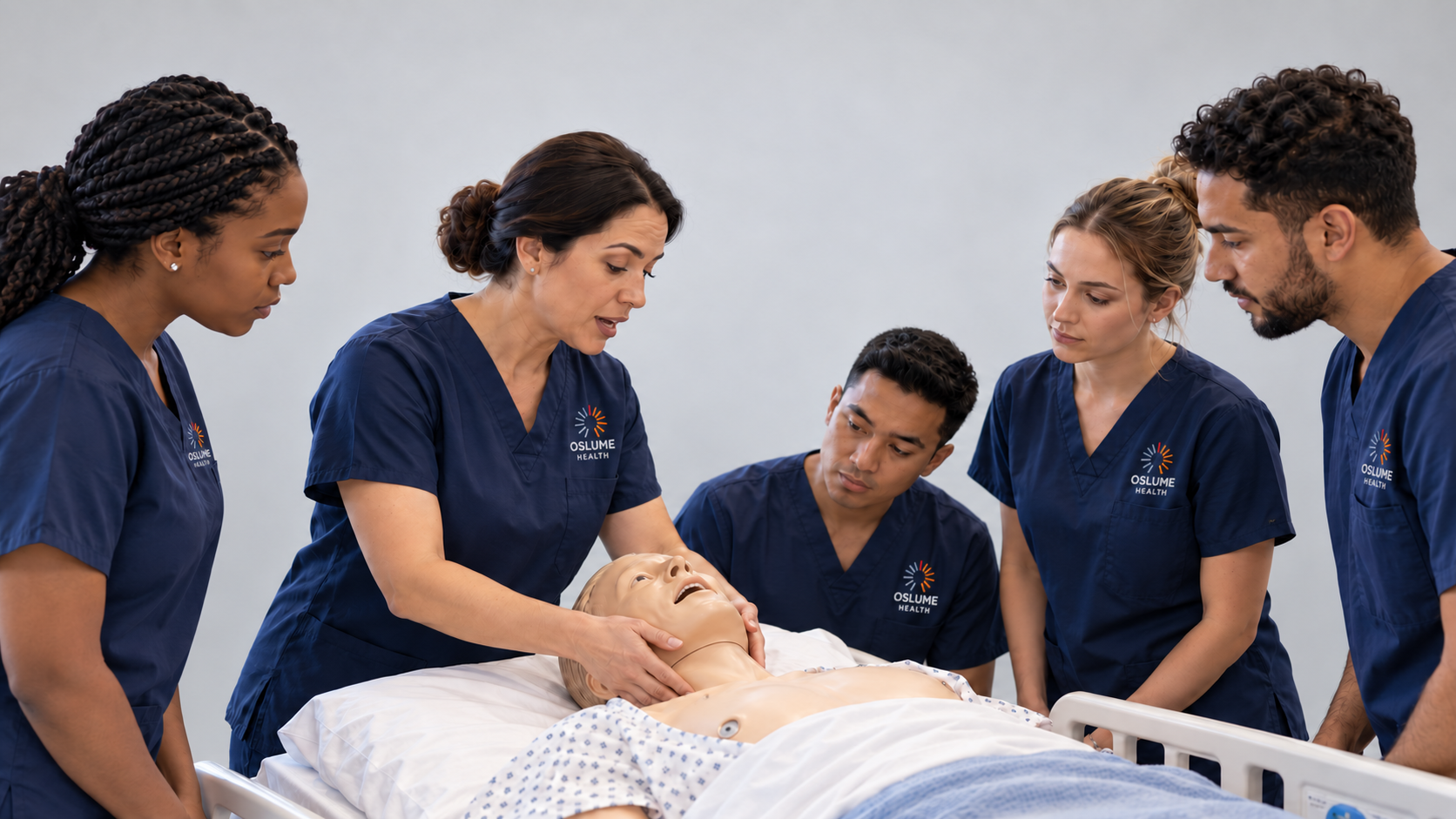 Oslume Health instructor demonstrating hands-on clinical skills with trainees in navy scrubs around a medical manikin